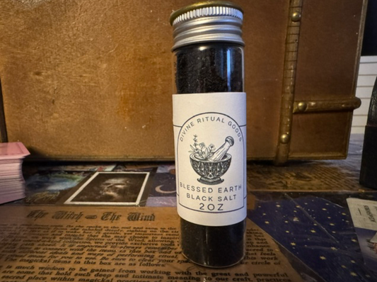 Bottle of 'Blessed Earth Black Salt' on a mystical-themed surface with books and tarot cards.