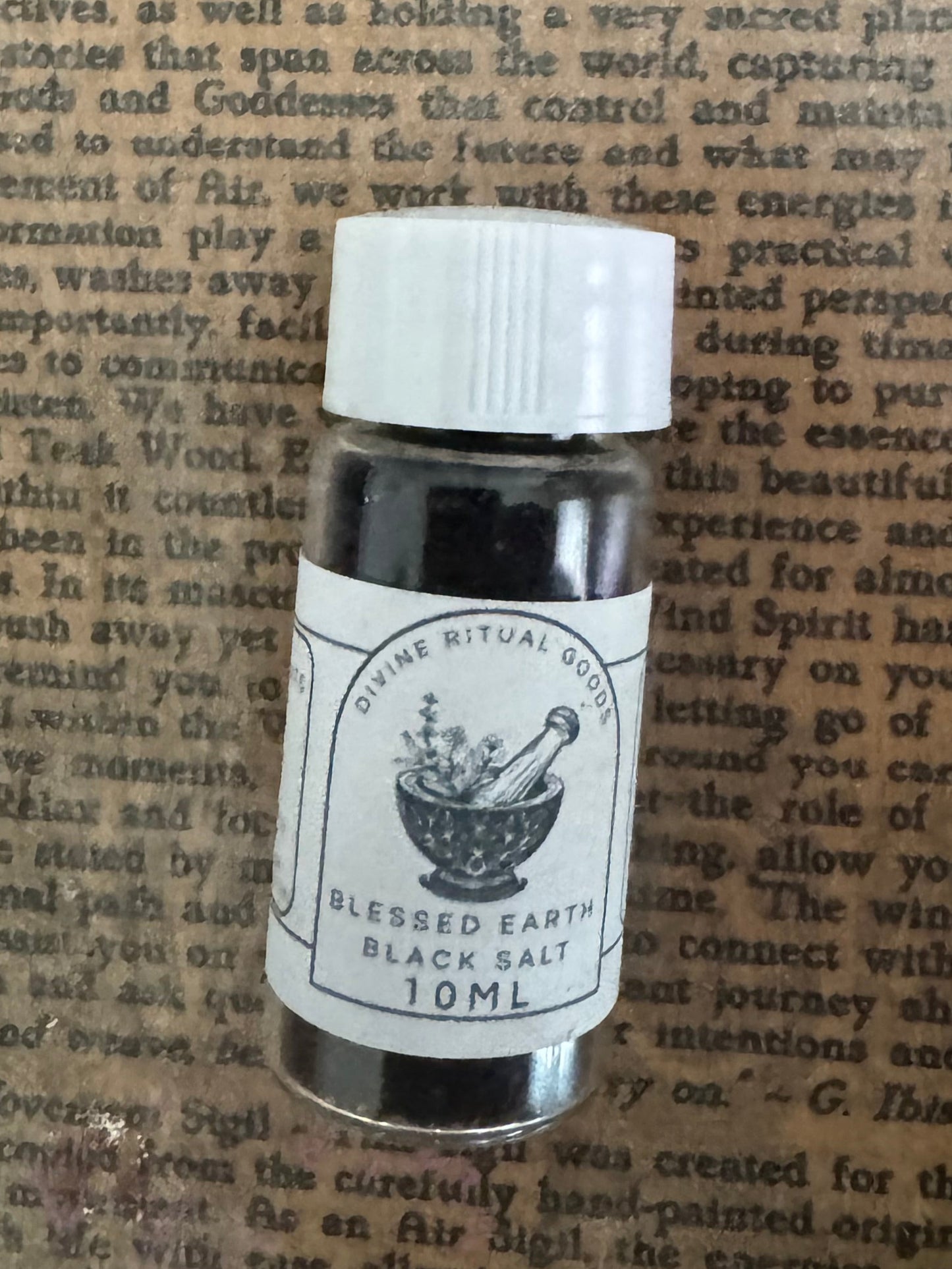 10 mL glass bottle of blessed black salt with a white cap on a textured paper background