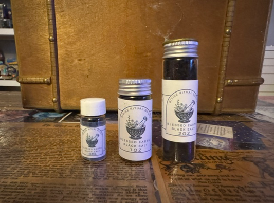 Three small bottles of blessed black salt on a surface with an old suitcase in the background